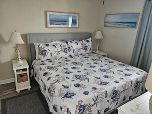 Une chambre d’hôtel comprenant un lit, deux tables de chevet, une petite table, un tapis et deux tableaux accrochés au mur.