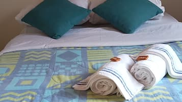 A bed with a patterned bedspread, two teal pillows, and a rolled white towel.
