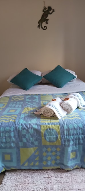 Una cama con una colcha estampada, dos almohadas color turquesa y una toalla blanca enrollada.