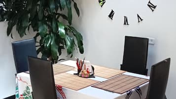A dining table with chairs, a clock on the wall, and a potted plant.