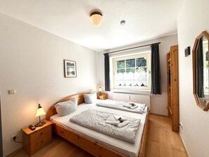 A bedroom with two beds, a bedside lamp, a window with curtains, a radiator, and a framed picture on the wall. - "oldsum 2, House 94" (Oldsum)