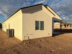 Ein eingeschossiges Haus mit einer beige farbenen Fassade, einem kleinen Fenster mit Fensterläden und einer Klimaanlage am Boden.
