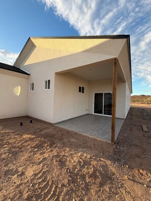 Een modern huis met een overdekte patio, een plat dak en een onverharde grond.