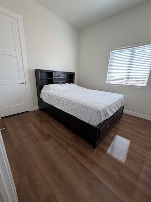 A bedroom with a bed, a door, a window with blinds, and a wooden floor. - Spacious 4-bedroom new construction house in fantastic Surprise with AC (Surprise)