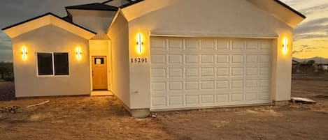 A two-story house with a garage, a driveway, and a dirt lot.