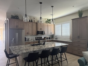 A modern kitchen with a large island, bar stools, and pendant lighting. - Winter Snowbird Retreat in Lake Havasu City, Arizona! Brand New Island Home (Lake Havasu City)