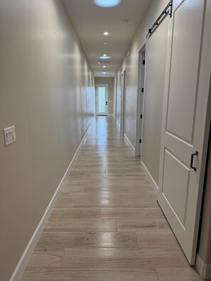 A hallway with wooden flooring, white walls, and doors on both sides. - Winter Snowbird Retreat in Lake Havasu City, Arizona! Brand New Island Home (Lake Havasu City)