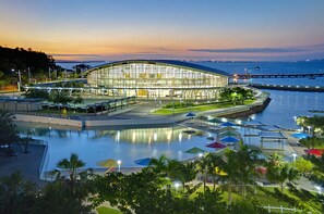 A modern building with a curved roof, surrounded by a waterfront promenade with umbrellas and lounge chairs. - Contemporary 1-bed Apartment Darwin CBD (Darwin)