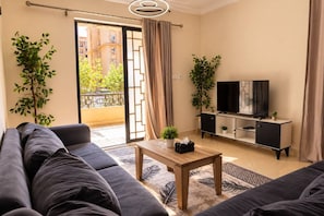 Un salon avec un canapé, une table basse, un téléviseur posé sur un meuble et un balcon agrémenté de plantes.
