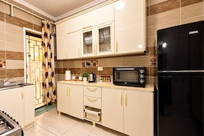 Une cuisine équipée d’un four à micro-ondes encastré, d’un réfrigérateur noir et d’une fenêtre avec un rideau.