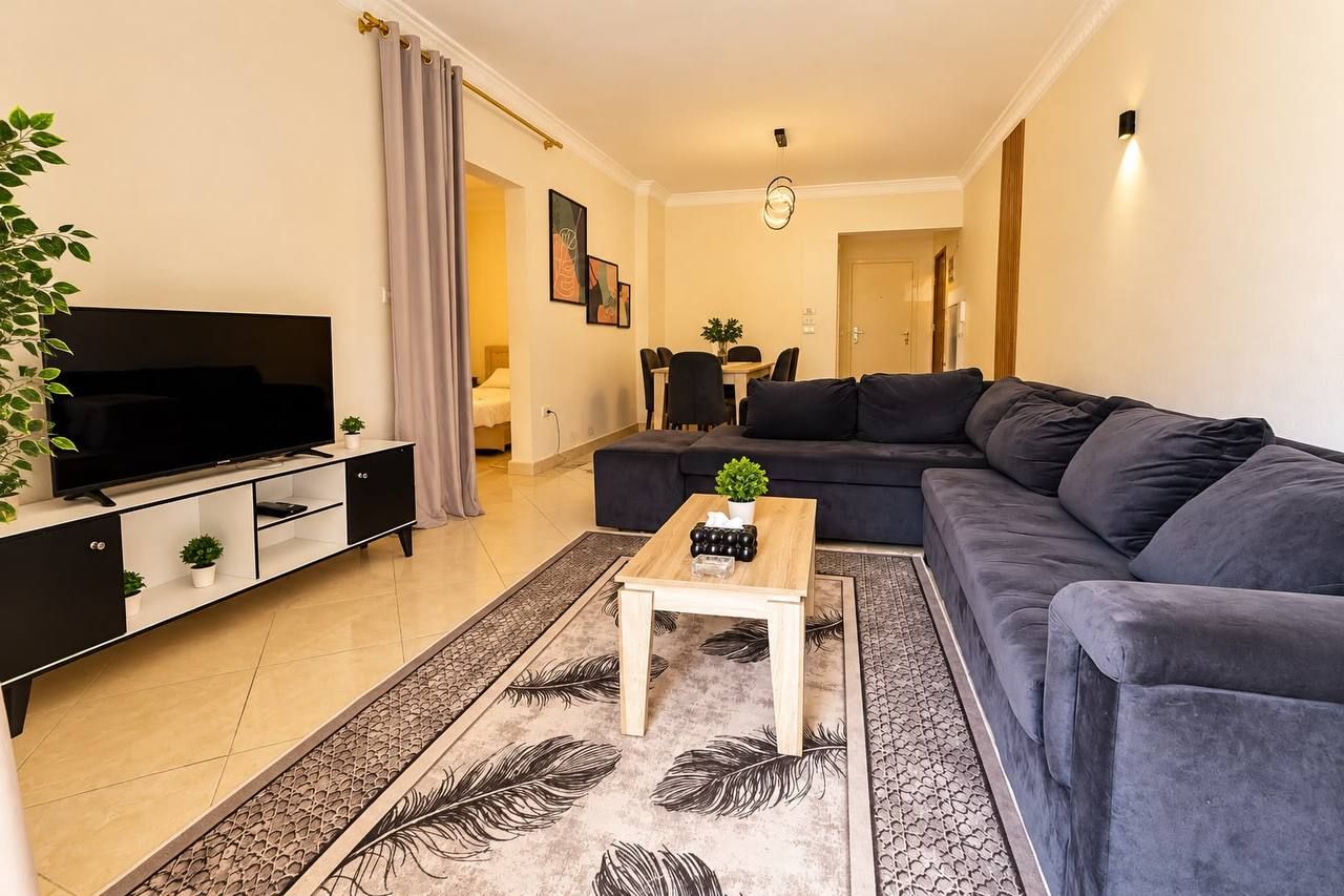 Un salon avec un canapé foncé, un téléviseur, une table basse et, au fond, un coin repas.
