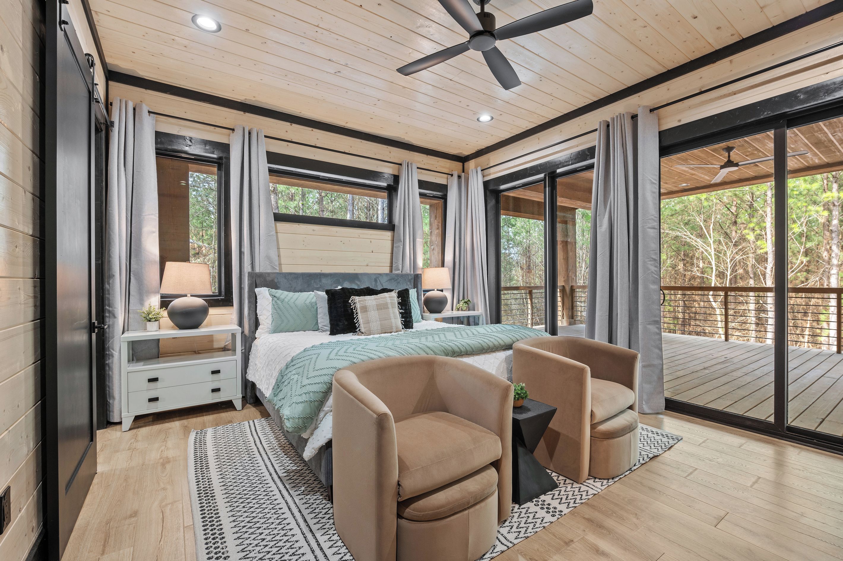 A bedroom with a bed, nightstands, a desk, a chair, and a view of the outdoors.