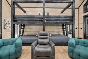 A bunk bed with a headboard, a reclining chair, and two armchairs in a cabin-style room with wooden walls and floors. - Sleeps 20 w/Playset·Arcade + Outdoor Pool Table (Broken Bow)