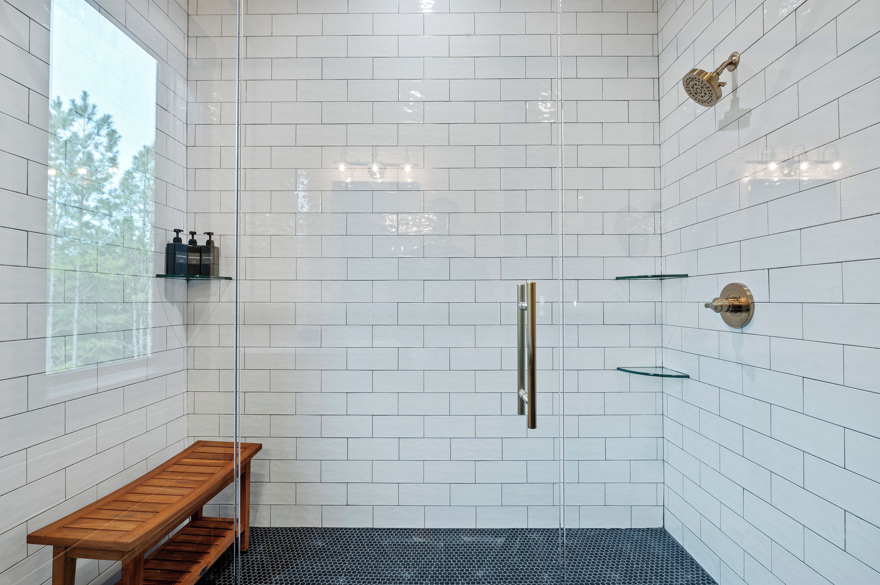 A shower with a glass door, a bench, and a shelf with toiletries.