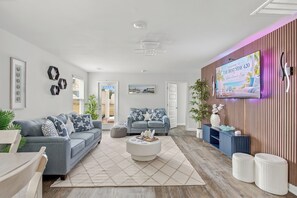 Ein modernes Wohnzimmer mit einem grauen Sofa, einem Couchtisch und einem an einer gestreiften Wand montierten Fernseher.