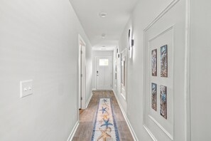 A hallway with a patterned rug, framed artwork on the walls, and a door at the end. - The Best Stay 420 - Cozy 4BR Home Near Savannah (Port Wentworth)
