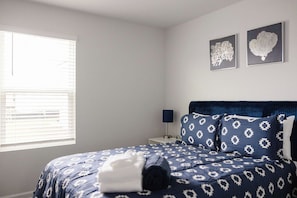 A bedroom with a bed, a nightstand, a lamp, and two wall art pieces. - The Best Stay 420 - Cozy 4BR Home Near Savannah (Port Wentworth)