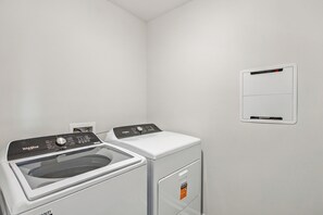 A laundry room with a Whirlpool washer and dryer, a white wall, and a thermostat on the wall. - The Best Stay 420 - Cozy 4BR Home Near Savannah (Port Wentworth)