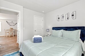 A bedroom with a bed, a nightstand, a wall-mounted lamp, and a door leading to a dining area. - The Best Stay 420 - Cozy 4BR Home Near Savannah (Port Wentworth)