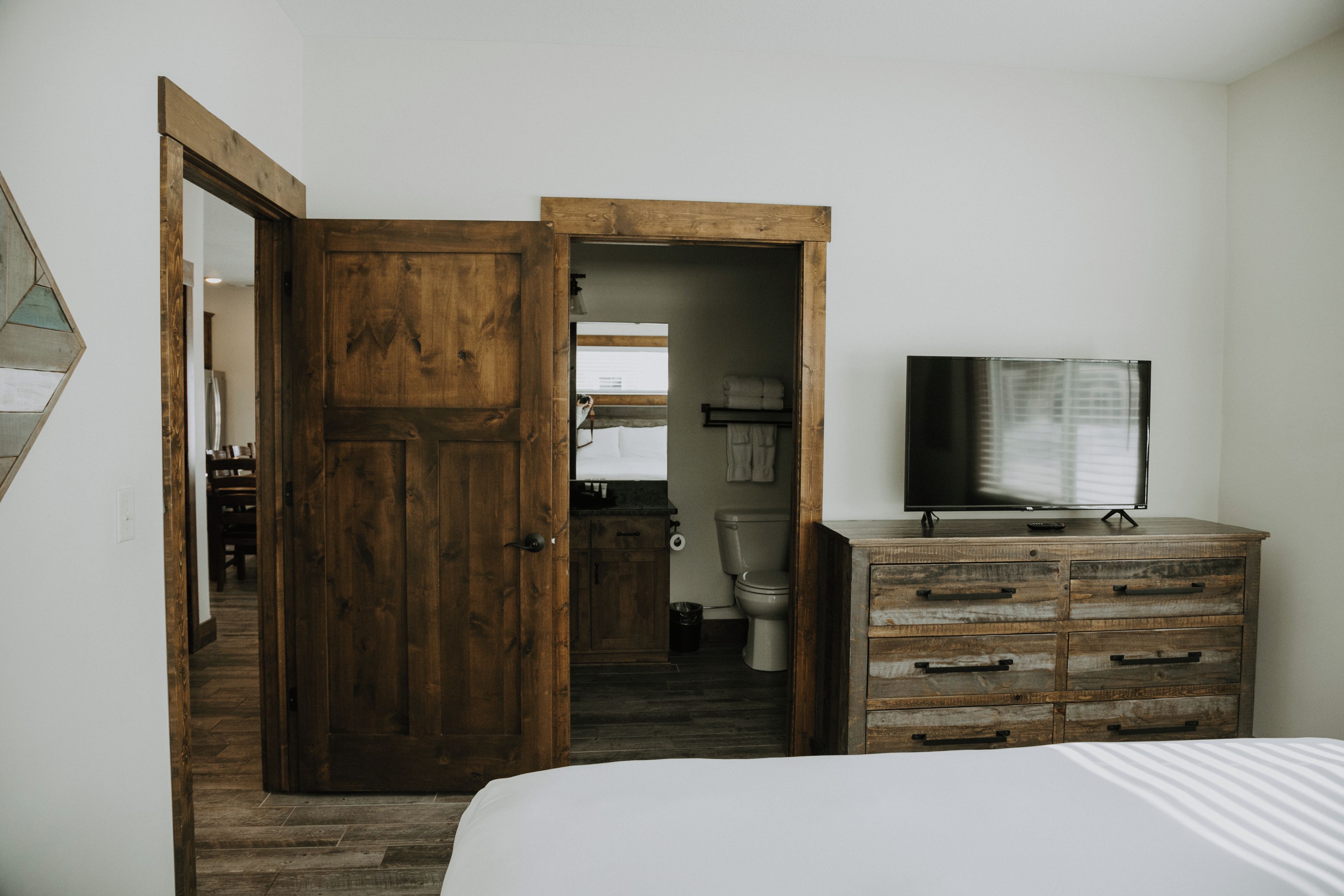 A bedroom with a wooden wardrobe, a bed, a television on a dresser, and a bathroom visible through an open door.