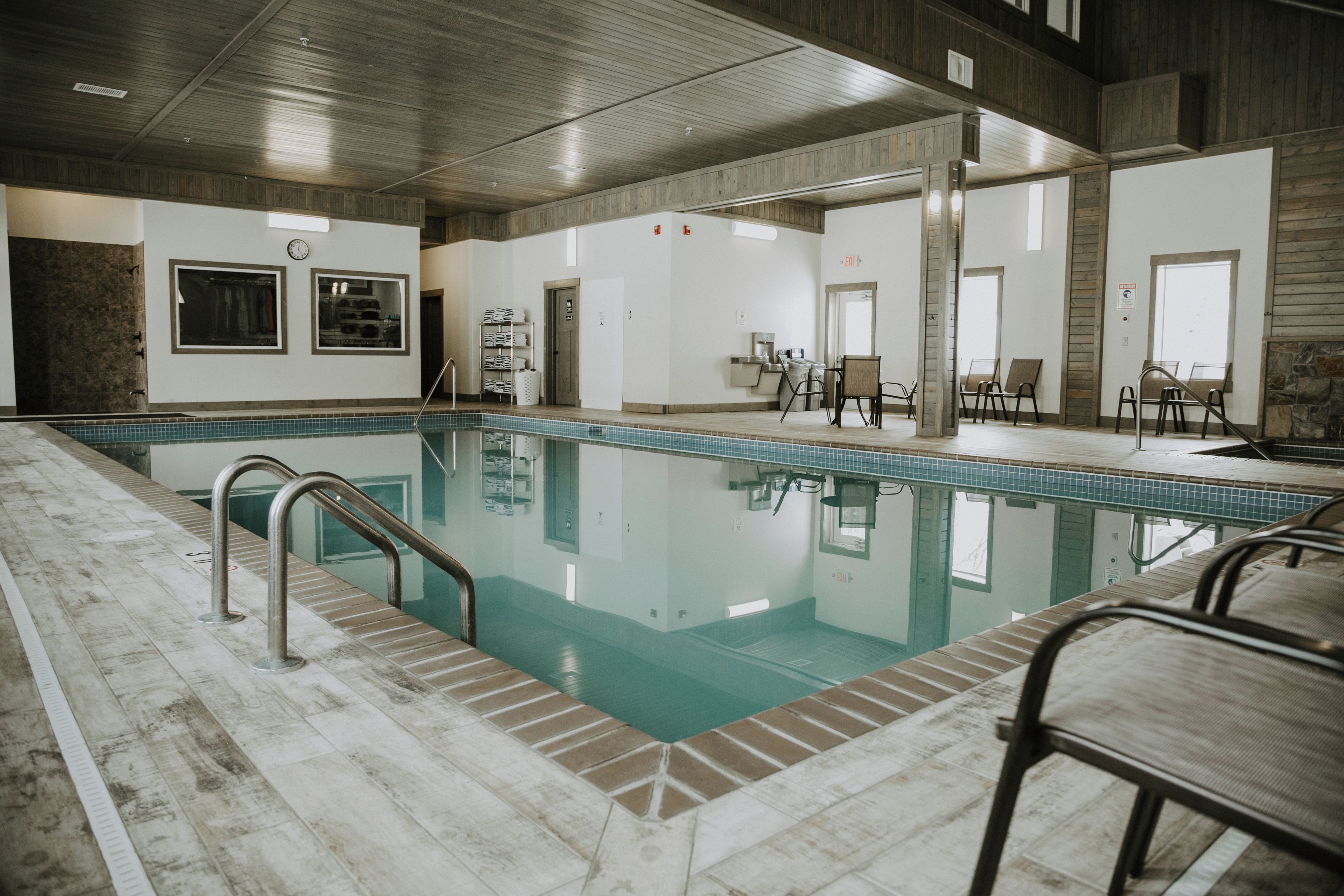 A swimming pool with a tiled deck, surrounded by a lounge area with chairs and a table.