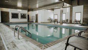 A swimming pool with a tiled deck, surrounded by a lounge area with chairs and a table.