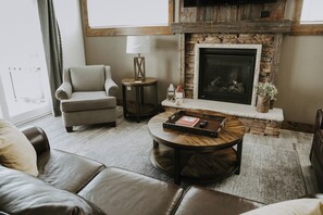 A living room with a stone fireplace, leather furniture, and a small side table with a lamp.