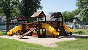 A playground with multiple slides and climbing areas, surrounded by grass and trees.
