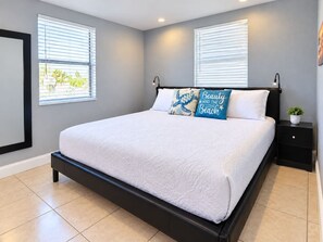 Une chambre à coucher avec un lit, deux tables de chevet et une fenêtre avec des stores.