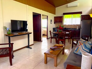 A living room with a TV, wooden furniture, a dining area with chairs, and a kitchen with cabinets. - (Bijagua de Upala)