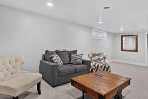 Un salon avec un canapé gris, un fauteuil à rayures, un fauteuil beige et une table basse en bois.
