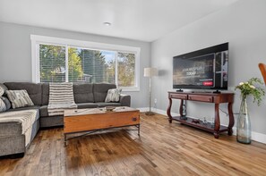 A living room with a sofa, coffee table, TV, and a floor lamp. - Newly Remodeled 4 Bedroom Townhome for 8 Guests (Billings)