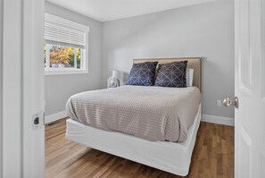 Une chambre avec un lit, une fenêtre, un ventilateur et une porte.
