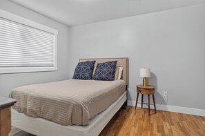 A bedroom with a bed, a bedside table, a lamp, and a window with blinds. - Newly Remodeled 4 Bedroom Townhome for 8 Guests (Billings)