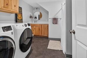 A laundry room with a front-loading washer and dryer, wooden cabinets, a mirror, and a towel rack. - Newly Remodeled 4 Bedroom Townhome for 8 Guests (Billings)