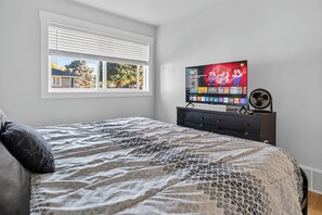 A bedroom with a bed, a TV on a stand, a window with blinds, and a wall-mounted fan. - Newly Remodeled 4 Bedroom Townhome for 8 Guests (Billings)