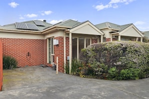 A residential building with a brick facade, a covered porch, and a large bush in the front yard. - Bright 1-bed House Near Thornbury Cafes (Melbourne)