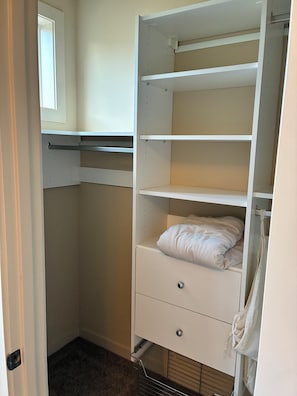 Een inloopkast met open planken, een kledingstang en een bed met een witte dekbedovertrek.