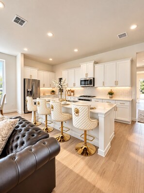 A modern kitchen with white cabinetry, stainless steel appliances, and a central island with bar stools.