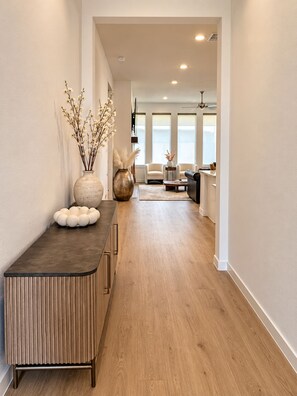 A modern interior with a wooden floor, a dark-toned console table, and a seating area with a sofa and chairs. - The Grand Haven (McKinney)