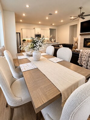 A modern living room with a dining area, a fireplace, and a kitchen in the background.