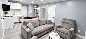 A modern living room with a grey sofa, a matching armchair, and a small round table with a candle and a box. - ATL Lakeview Haven - Private Suite & Deck (Decatur)