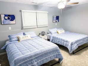 Een slaapkamer met twee bedden, een plafondventilator en kunstwerken aan de muren.