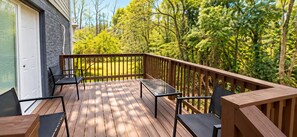 A wooden deck with outdoor furniture, a glass table, and a view of a forested area. - ATL Lakeview Haven - Private Suite & Deck (Decatur)
