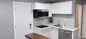 A compact kitchen with white cabinetry, a built-in microwave, a herringbone-patterned backsplash, and a dishwasher. - ATL Lakeview Haven - Private Suite & Deck (Decatur)