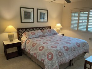 A bedroom with a bed, two nightstands, two lamps, a ceiling fan, and two framed pictures on the wall. - Palm Desert Golf Course Home (Palm Desert)
