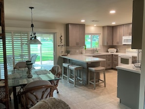 A modern kitchen with a dining area, featuring a large island with bar stools, a built-in oven, and a view of the outdoors. - Palm Desert Golf Course Home (Palm Desert)