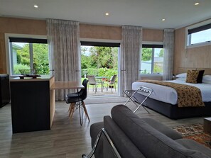 A modern hotel room with a bed, a sofa, a dining area, and a view of the outdoors.