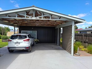 A covered garage with a white car parked inside, a wooden fence, and a metal gate.