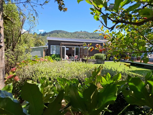 A modern house with a patio, surrounded by lush greenery and a clear view of a hill.
